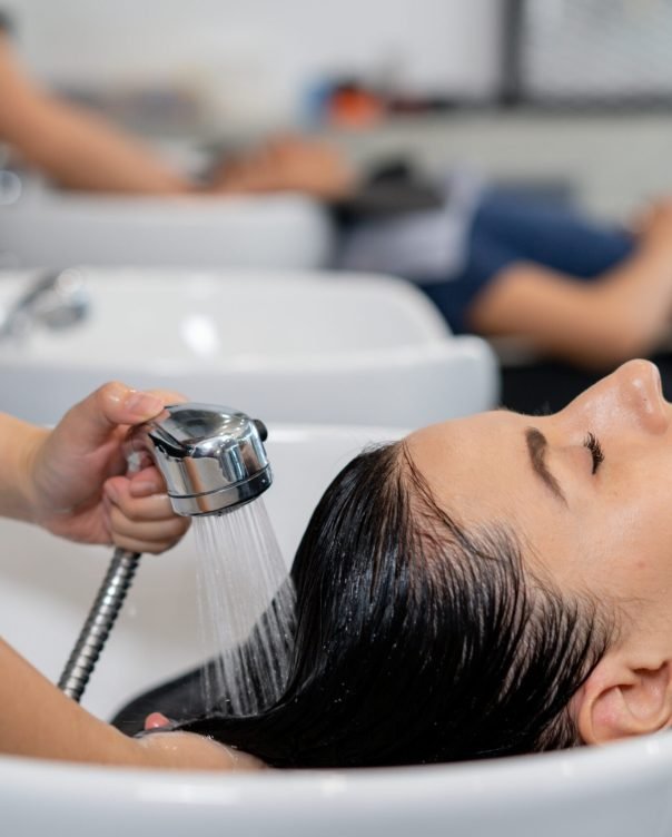 Young Caucasian woman at the hairdresser pampering herself by getting her hair washed and rinsed with eyes closed with head in sink for hairwash